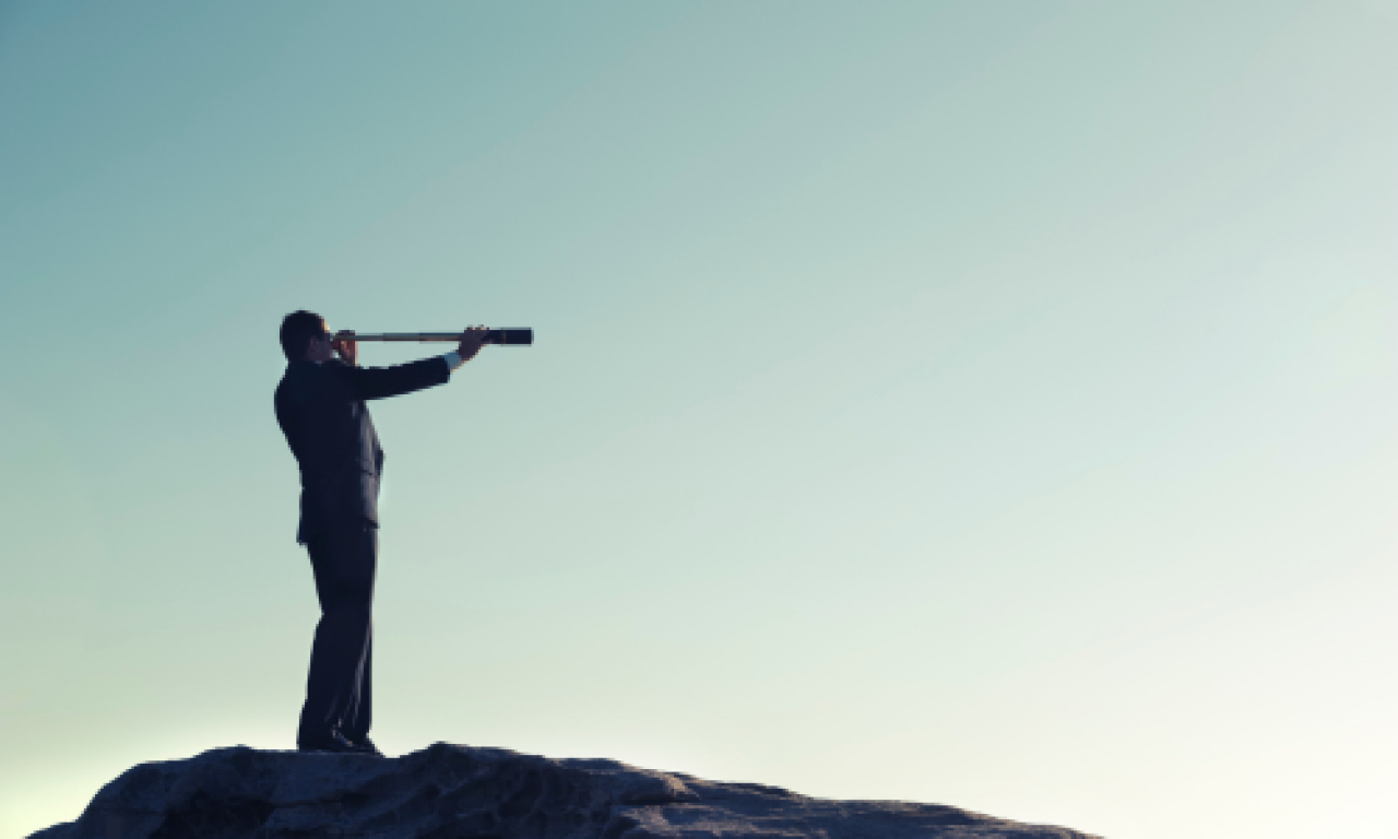 Business man on a rock with a telescope looking through it, with a clear sunrise behind.